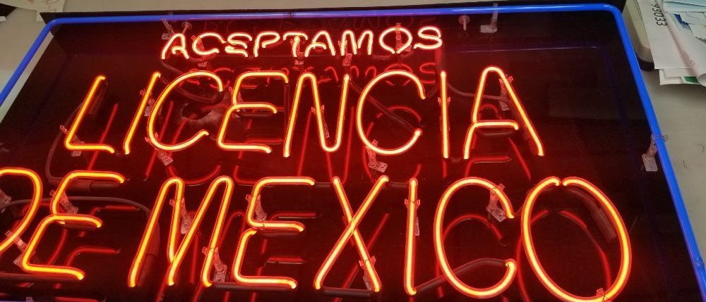 A red neon sign reading "Aceptamos Licencia de Mexico" in a blue frame, laid on the work table.
