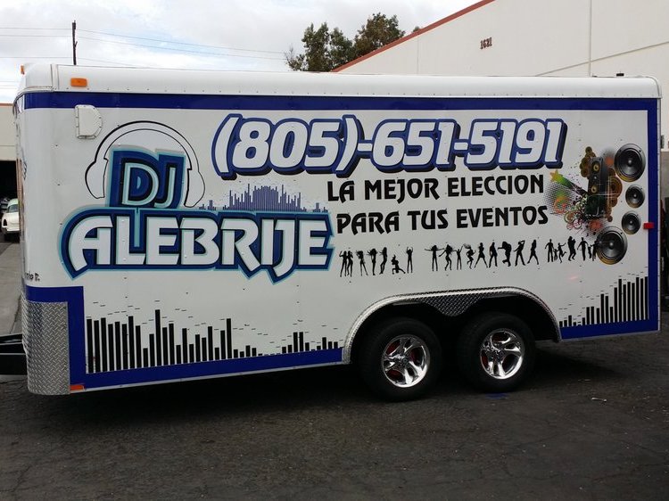 A white tandem-axle cargo trailer wrapped along its side with a DJ logo, a phone number, a Spanish slogan and dancer silhouettes.
